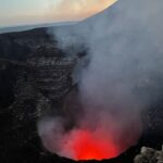 Lava inside Volcan Masaya in Nicaragua. You can see bright orange lava inside the circular crater, with thick grey smoke rising out of it. The orange sunset can just about be seen in the background, although it's tricky to fully make out with all the smoke in the way