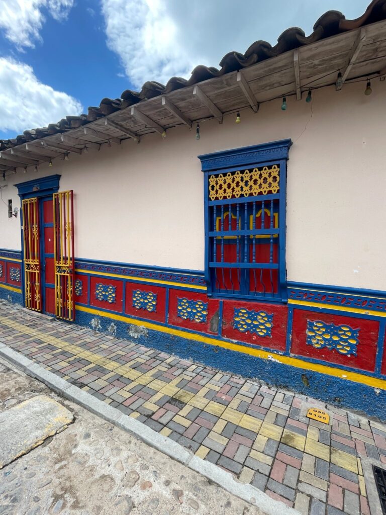 A white building in Guatape with blue windows and colourful zocalos painted in red and blue.