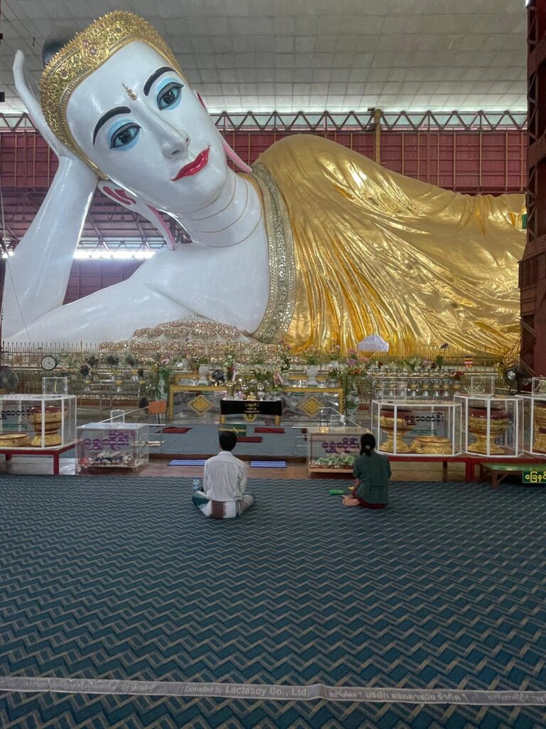 The reclining Buddha at Chaukhtatgyi Buddha Temple, with worshippers praying in front.