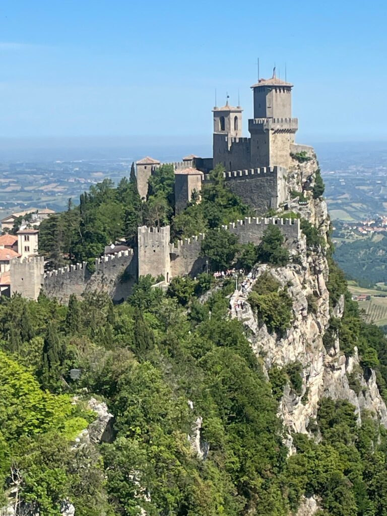 The Guaita Tower in San Marino: a castle surrounded by walls which is located on top of a giant rockface covered in greenery.