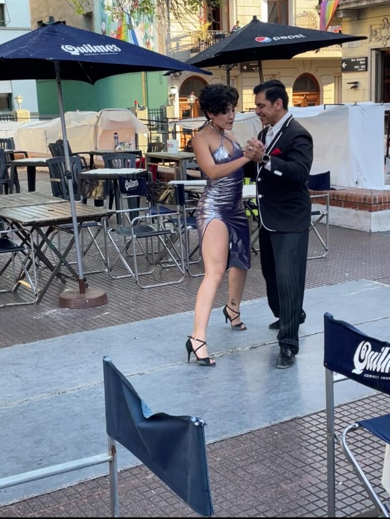 A man in a suit and a woman in a purple dress dancing tango in Plaza Dorrego, San Telmo, Buenos Aires.