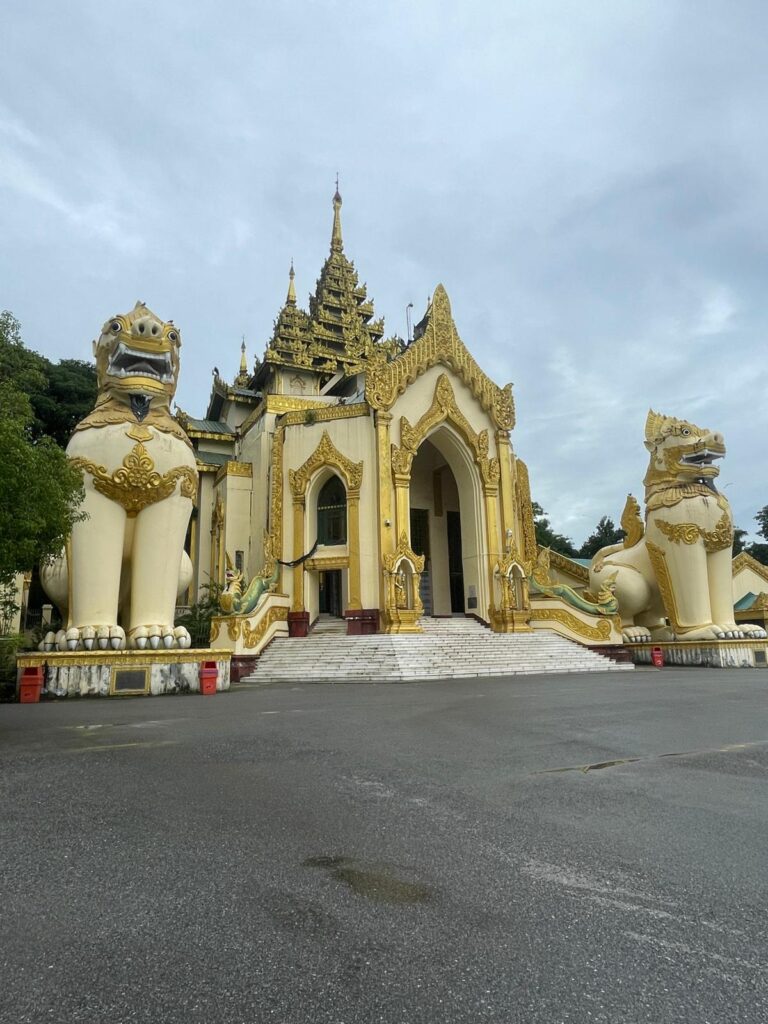 The entrance to Shwedagon Pagoda, Myanmar's most famous Buddhist site which is based in Yangon. The entrance is gold, with two statues of chinthe (mythical lion-like creatures) standing either side.