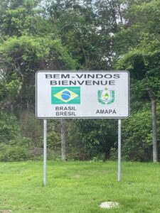 A sign at the French Guiana/Brazil border that says "Bem-Vindos - Bienvenue" ("welcome" in both Portuguese and French) alongside the flag of Brazil and the logo of Amapa (the Brazilian state that borders French Guiana).