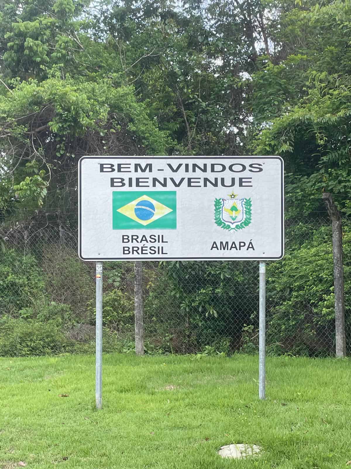 A sign at the French Guiana/Brazil border that says "Bem-Vindos - Bienvenue" ("welcome" in both Portuguese and French) alongside the flag of Brazil and the logo of Amapa (the Brazilian state that borders French Guiana).