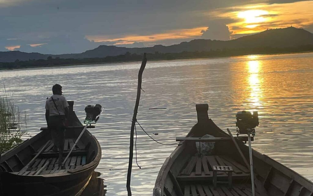 Two boats in the foreground as the sun sets over the Irrawaddy River in Myanmar