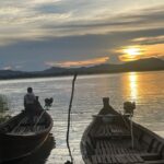 Two wooden boats on the Irrawaddy River in Bagan, Myanmar. A local stands on the left boat as the sun sets across the water