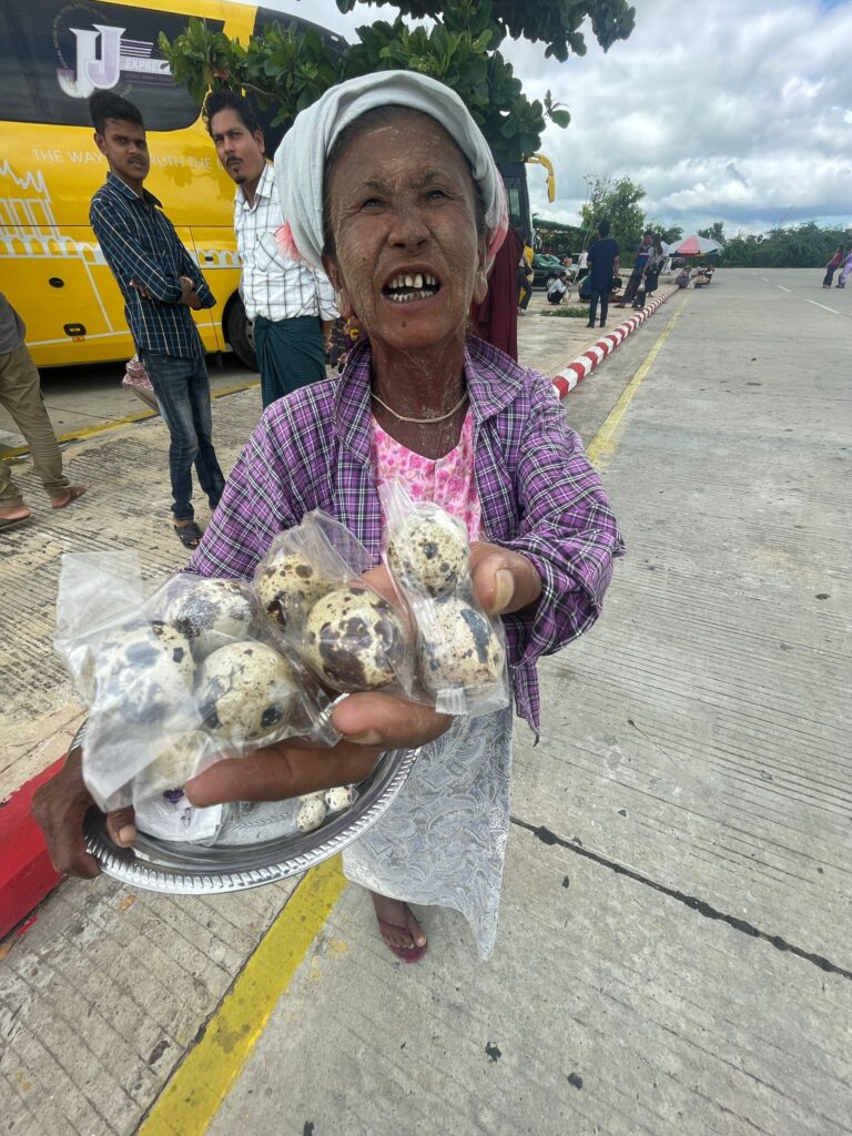 A Burmese lady with traditional Burmese head cloth (gaung baung) on her head and thanaka (a popular Burmese cosmetic) on her face, which is a form of white powder. She is holding a bag of small eggs