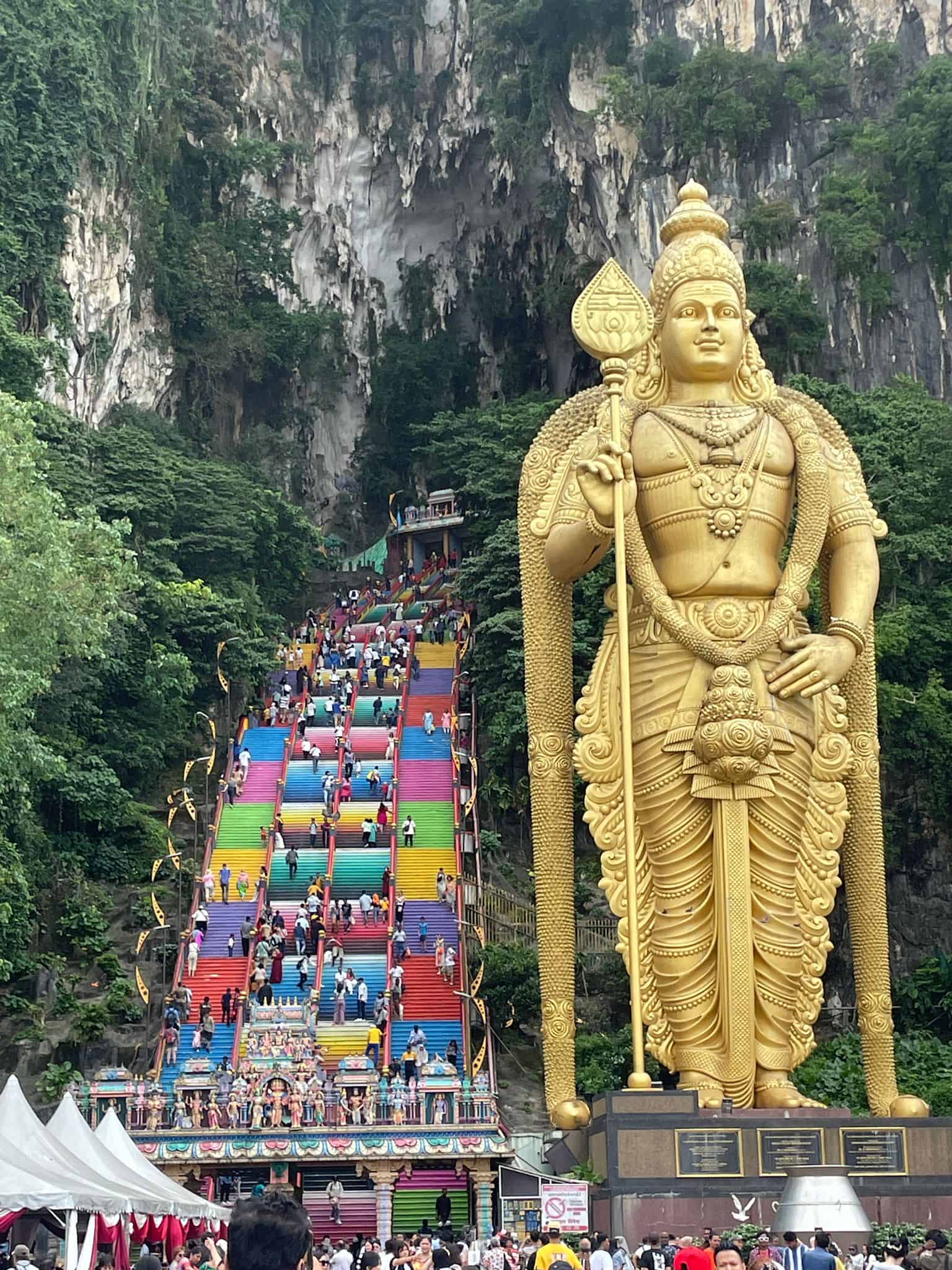 The iconic giant gold statue of Lord Murugan standing beside the colourful steps at Kuala Lumpur's Batu Caves.