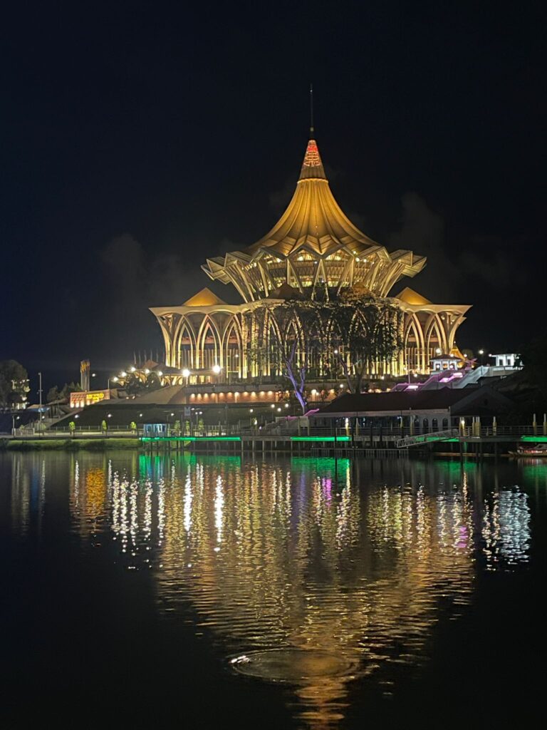 The Sarawak State Legislative Assembly building lit up and reflecting off the water at night in Kuching, Malaysia