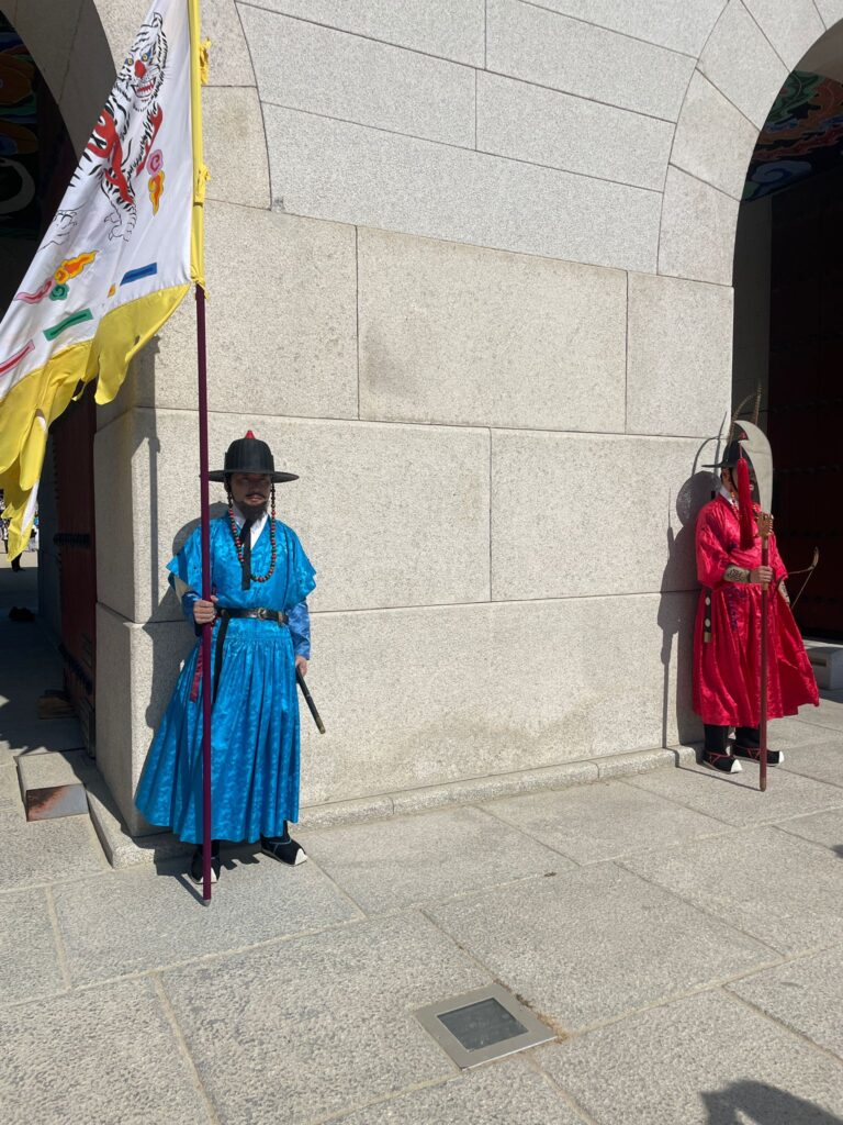 Two guards wearing traditional Korean hanboks (blue on the left, red on the right) as they guard the gates to Seoul's Gyeongbokgung Palace