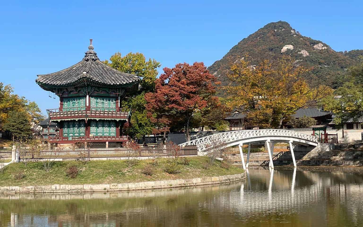 A traditional piece of Korean architecture to the left of a white bridge over a small river at Gyeongbokgung Palace, Seoul, South Korea