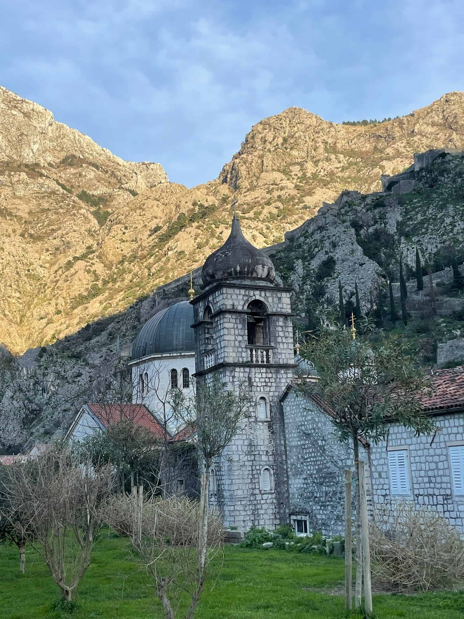 A cathedral in Kotor's Old Town (Montenegro) with mountains in the background and grass in the foreground
