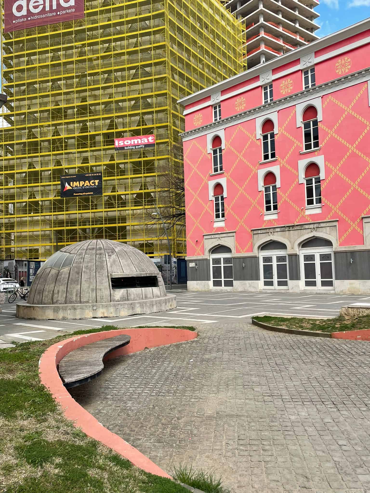 One of Albania's infamous bunkers standing in front of a pink building in Tirana, Albania