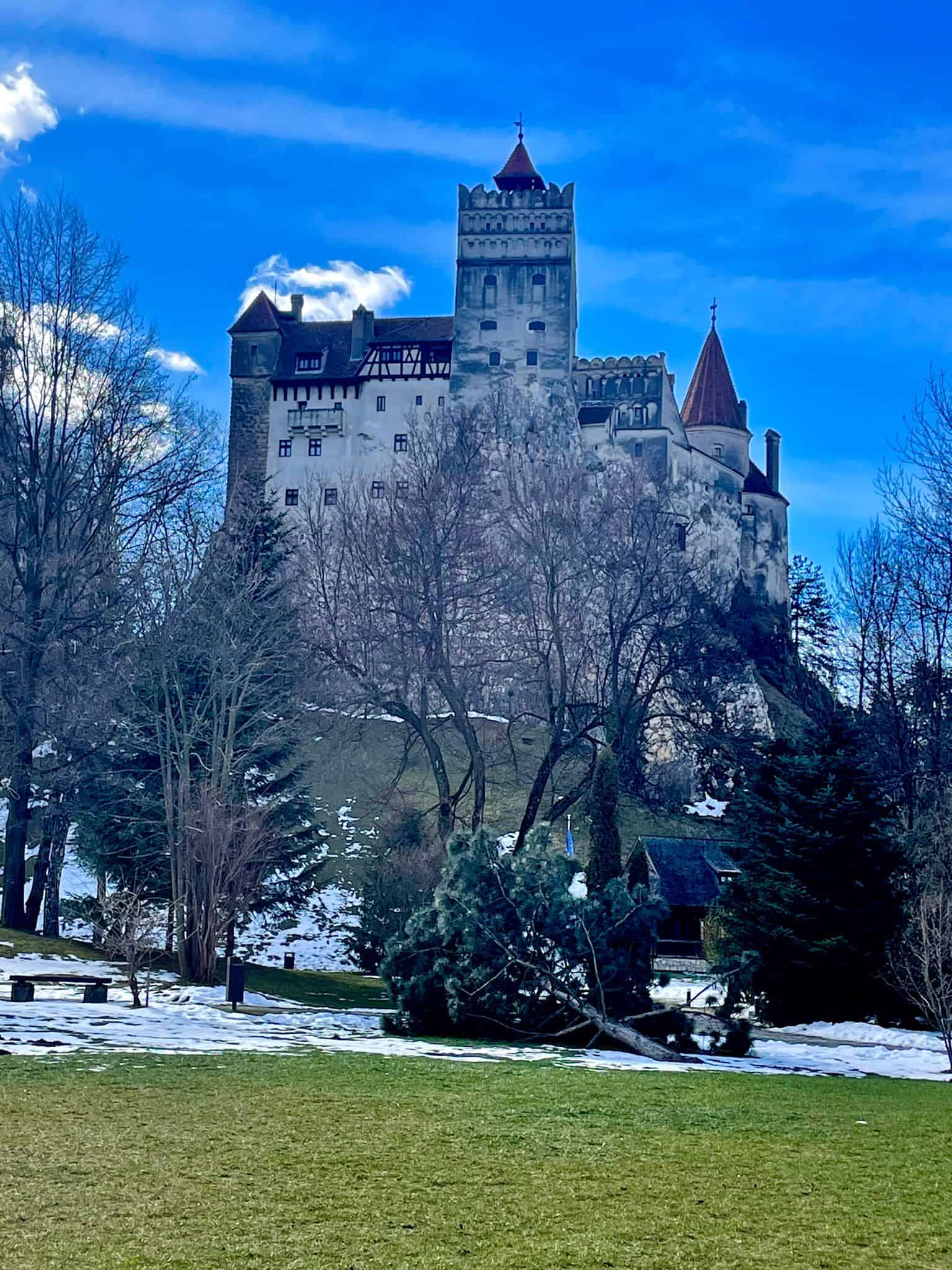 Bran Castle (Dracula's Castle) in Romania with snow and grass in the foreground and dark blue skies