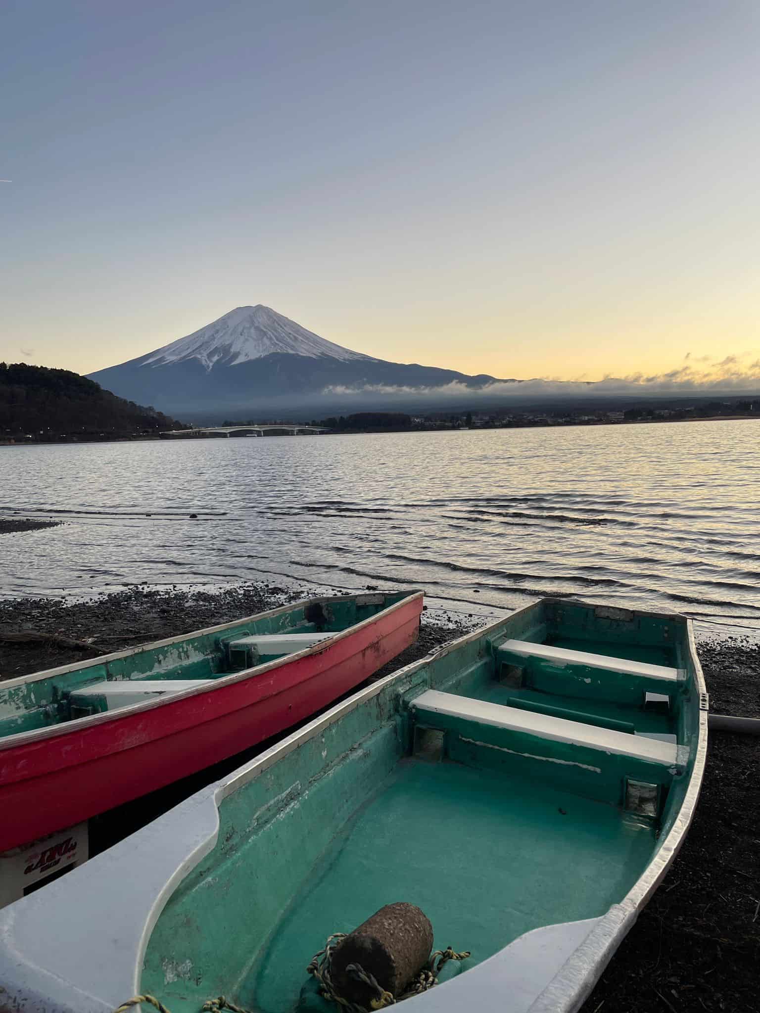 Mount Fuji at sunset with a couple of boats in the foreground and a lake separating them from the volcano