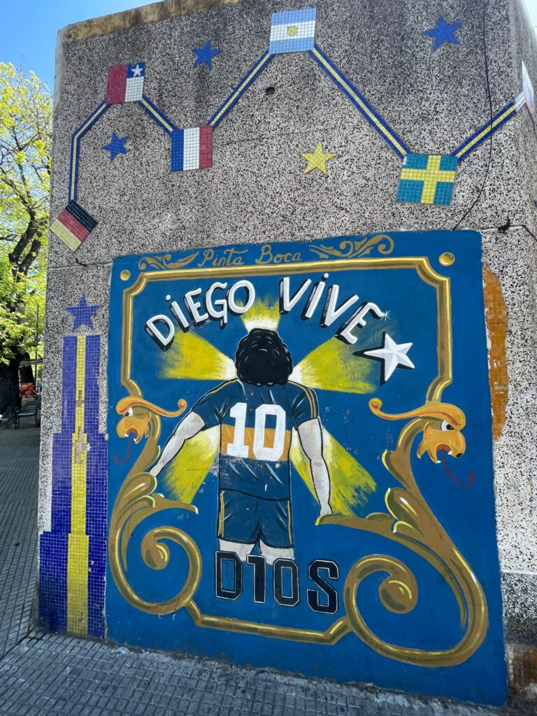 Street art paying tribute to football legend Diego Maradona. This image shows Maradona in a Boca Juniors shirt with the number ten on the back, looking towards a shining light in the distance
