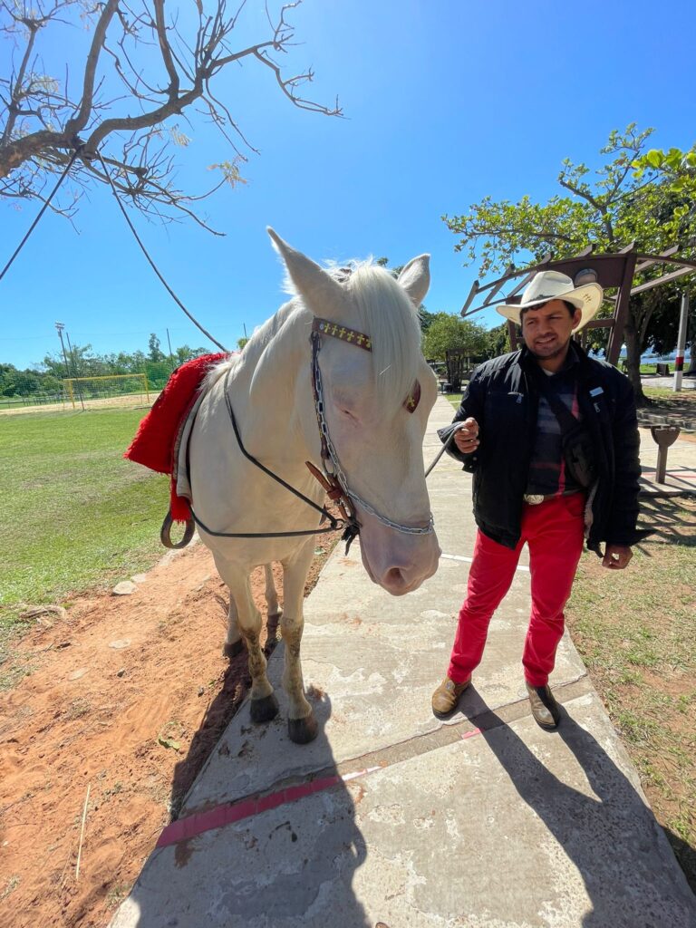 A Paraguayan man in a Panama hat with his white horse in the sun surrounding Aregua