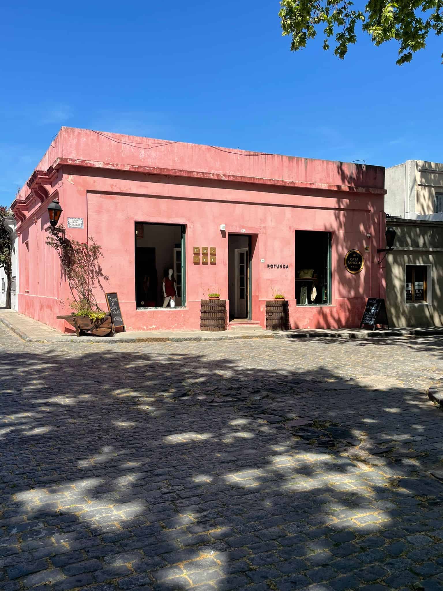 A pink pastel-coloured building in Colonia del Sacramento, Uruguay, with a couple of small trees outside as the sun shines down