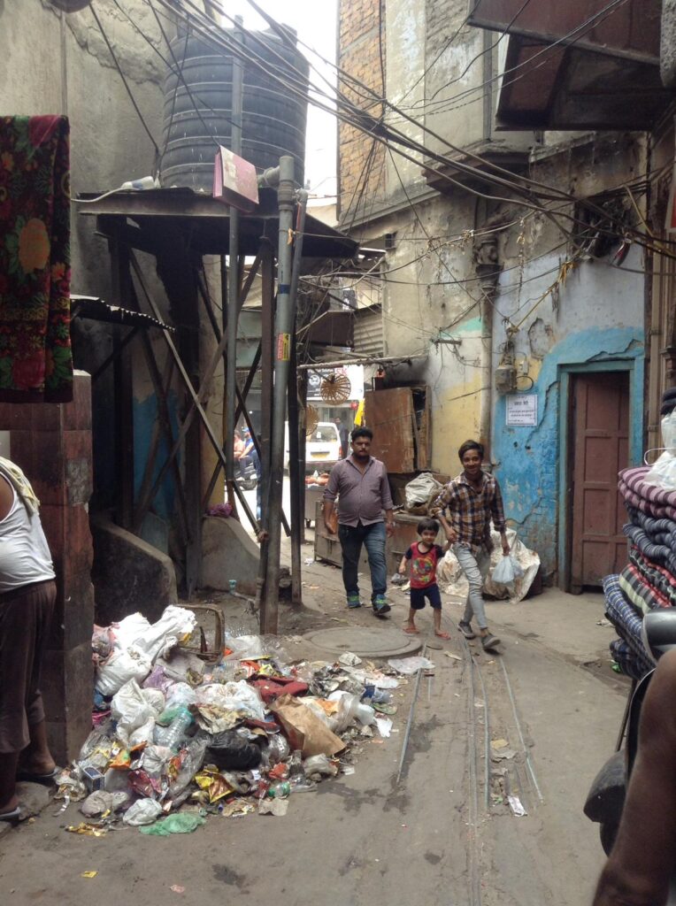 A group of Indians walk through a narrow alleyway alongside a giant pile of rubbish in Paharganj: the number one destination in New Delhi for anyone backpacking India