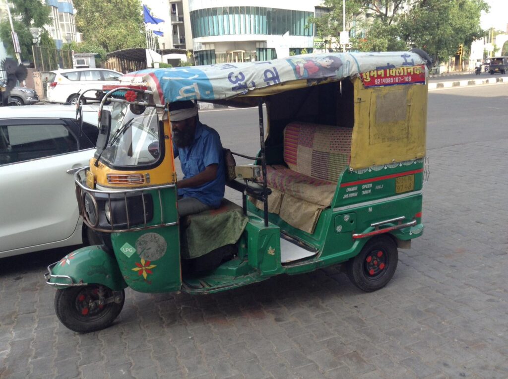 A bearded man driving a green and yellow tuk tuk in India