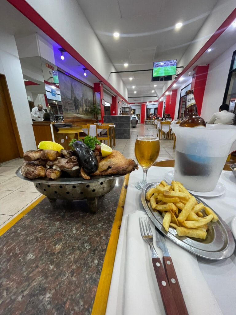 An Argentine asado including various cuts of meat alongside chips and a large bottle of Quilmes beer