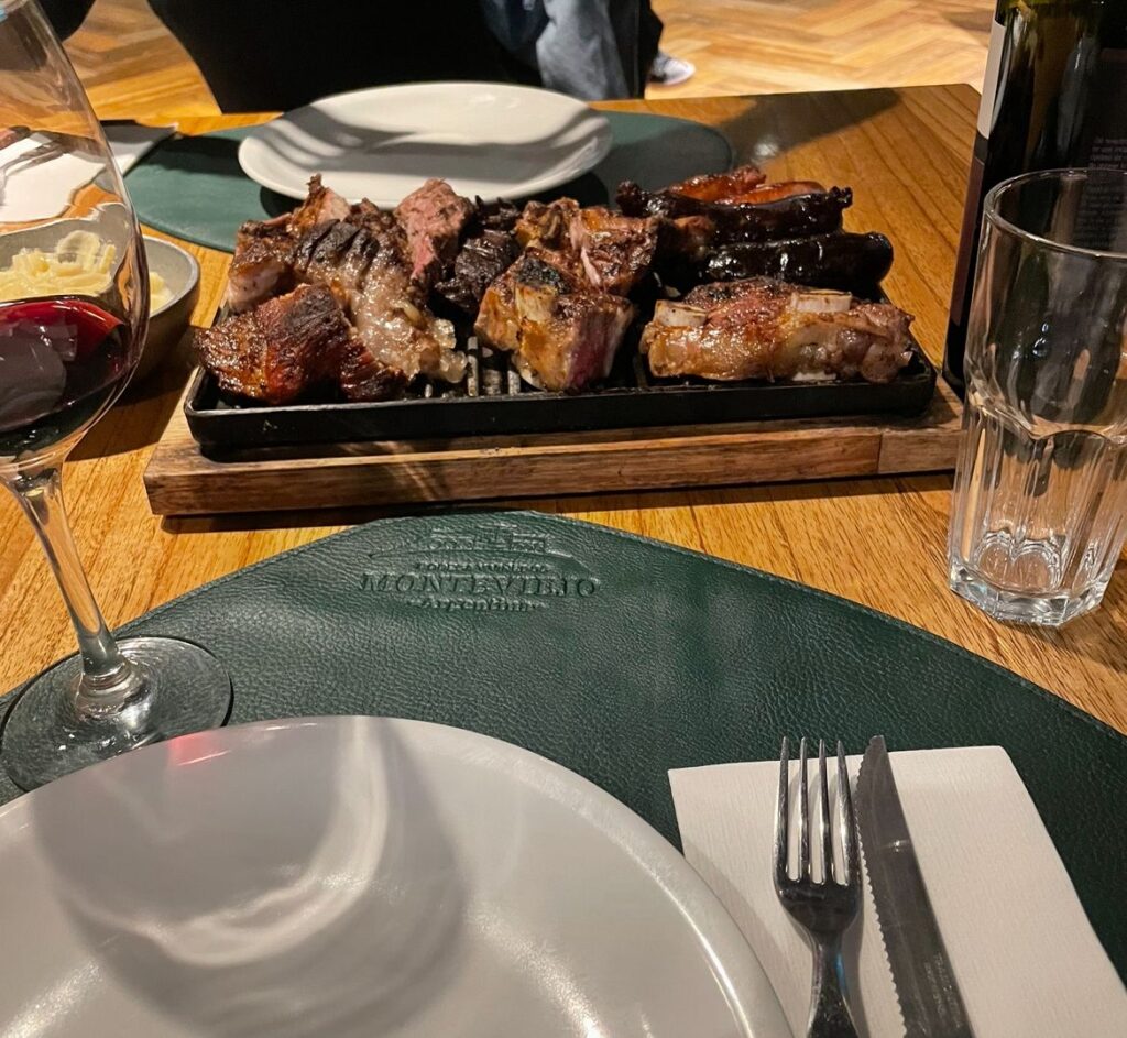 A series of meats at El Asadito steakhouse in Mendoza. Popular cuts including tira de asado and morcilla sausages are included alongside a glass of local Malbec wine