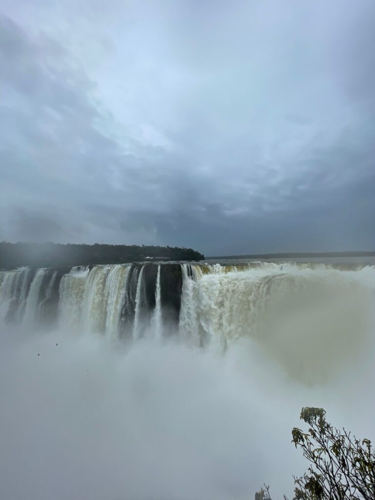 Waterfalls crashing down at Iguazu Falls in Argentina with a huge cloud of mist ascending from the river below and grey clouds in the skies during a very rainy day
