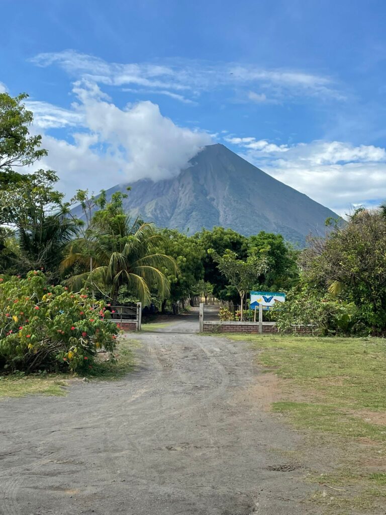 Volcan Concepcion on Ometepe Island looms over the entrance to Charco Verde Wildlife Reserve. A dirt path through the trees separates the reserve from the volcano, which has clouds colliding with its tall peak