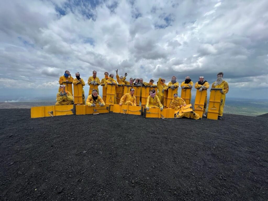 My 21-strong tour group all wearing yellow protective jumpsuits and safety goggles whilst holding yellow boards which we would use to board down Cerro Negro Volcano (with the black ash pictured in the foreground) just after this photo was taken
