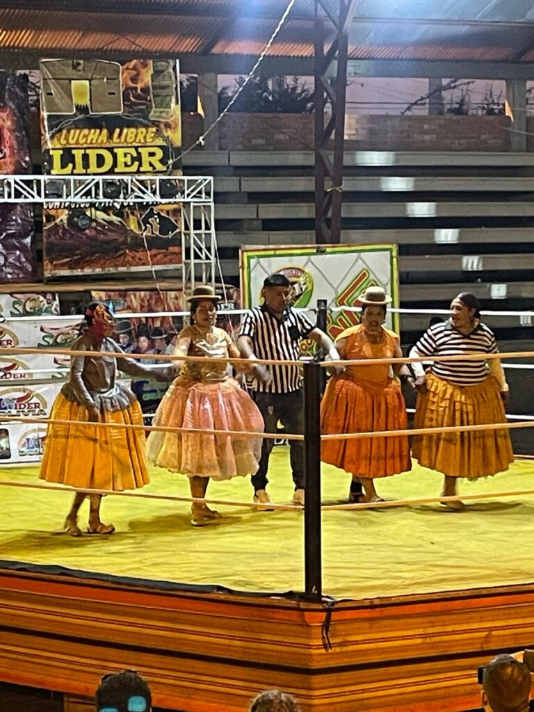 Four cholitas (Bolivian ladies in traditional clothing including bowler hats and puffy skirts) standing either side of a referee during the cholita's wrestling event in El Alto