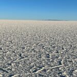 The white salt flats of Uyuni in Bolivia, with a clear blue sky in the background and the silhouette of some mountains in the background.