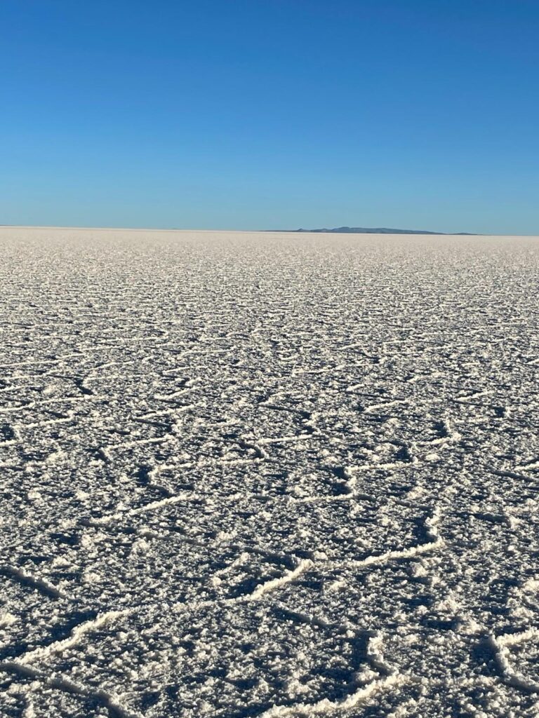 Plain white salt flats in Bolivia with a blue sky and the outline of mountains inbetween