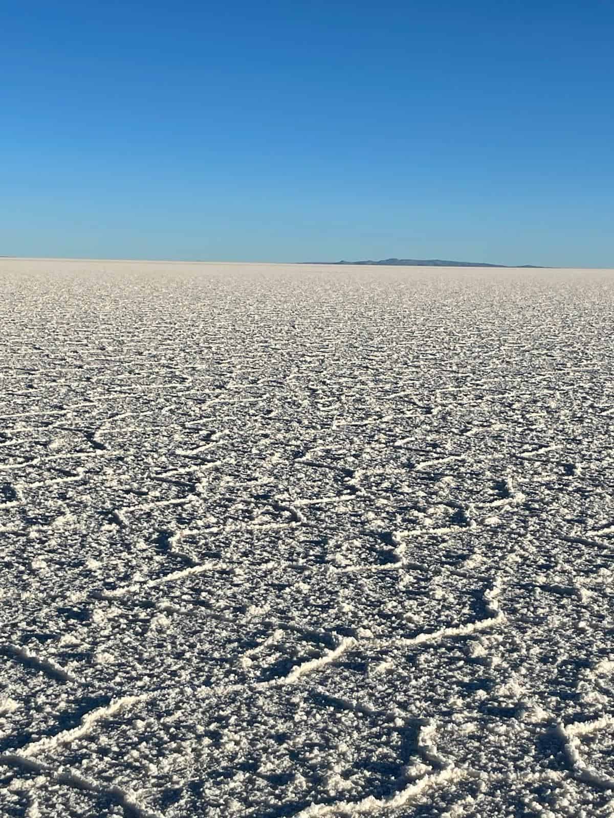 The white salt flats of Uyuni in Bolivia, with a clear blue sky in the background and the silhouette of some mountains in the background