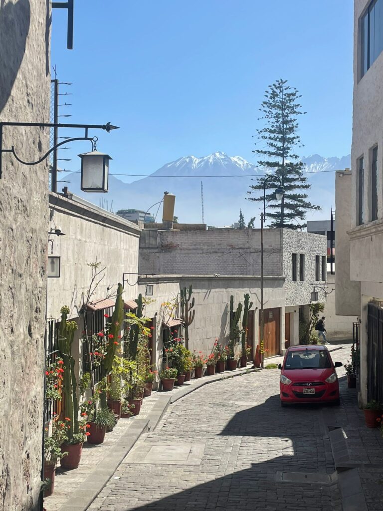 Arequipa's streets in Peru, with snow-capped mountains in the background and a red car on the road alongside some green plants including cacti