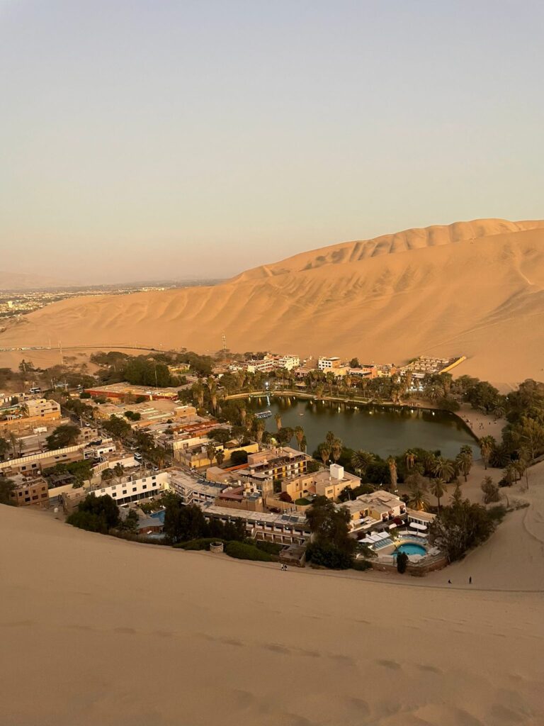 A pond surrounded by many buildings in the middle of the sand dunes which make up Huacachina, a desert oasis in Peru