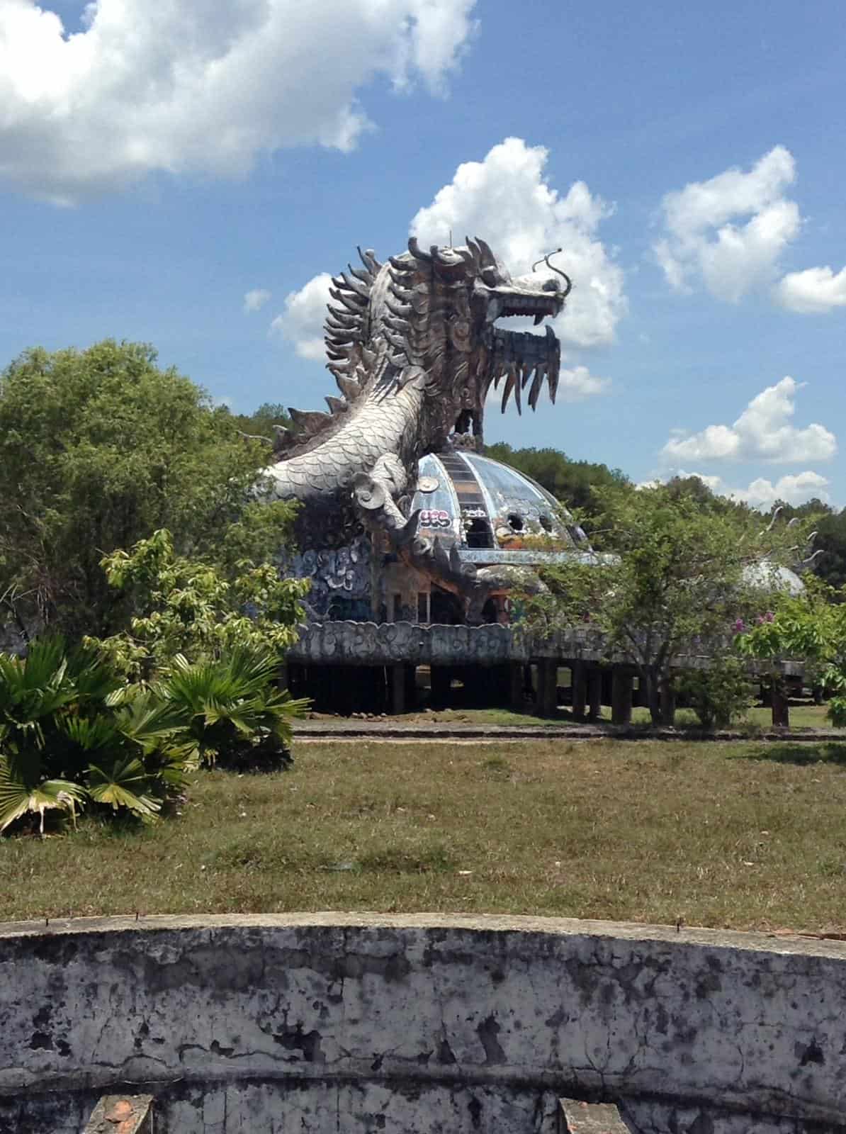 A dragon statue at Ho Thuy Tien, an abandoned water park in Hue, Vietnam. The dragon is the centerpiece of the park and you can walk up inside it and reach the dragon's mouth from where you can see most of the park. In this image, there is dry grass and many trees surrounding the dragon, although it is also surrounded by a dried-up lake 