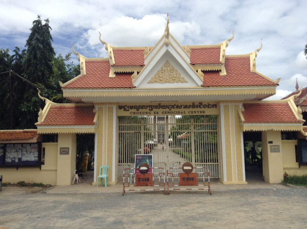 A colourful yellow and red archway in traditional Cambodian style with several "horns" poking out of the sides. This particular archway is the entrance to Choeung Ek Genocidal Center, otherwise known as the Killing Fields. This is because it was the scene of many executions during the communist Khmer Rouge era