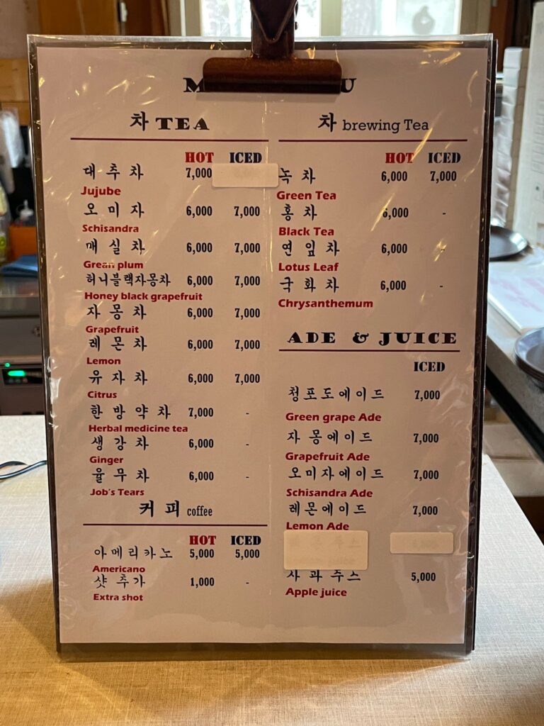 A menu for the cafe outside the entrance to Beopjusa Temple. It sells the following with prices in Korean Won:

Tea:
Jujube (₩7,000 hot)
Schisandra (₩6,000 hot, ₩7,000 iced)
Grean plum (₩6,000 hot, ₩7,000 iced)
Honey black grapefruit (₩6,000 hot, ₩7,000 iced)
Grapefruit (₩6,000 hot, ₩7,000 iced)
Lemon (₩6,000 hot, ₩7,000 iced)
Citrus (₩6,000 hot, ₩7,000 iced)
Herbal medicine tea (₩7,000 hot)
Ginger (₩6,000 hot)
Job's Tears (₩6,000 hot)

Brewing tea:
Green tea (₩6,000 hot, ₩7,000 iced)
Black tea (₩6,000 hot)
Lotus Leaf (₩6,000 hot)
Chrysanthemum (₩6,000 hot)

Coffee:
Americano (₩5,000 hot, ₩5,000 iced)
Extra shot (₩1,000)

Ades and juices (all iced):
Green grape ade: (₩7,000)
Grapefruit ade (₩7,000)
Schisandra ade (₩7,000)
Lemonade (₩7,000)
Apple juice (₩5,000)