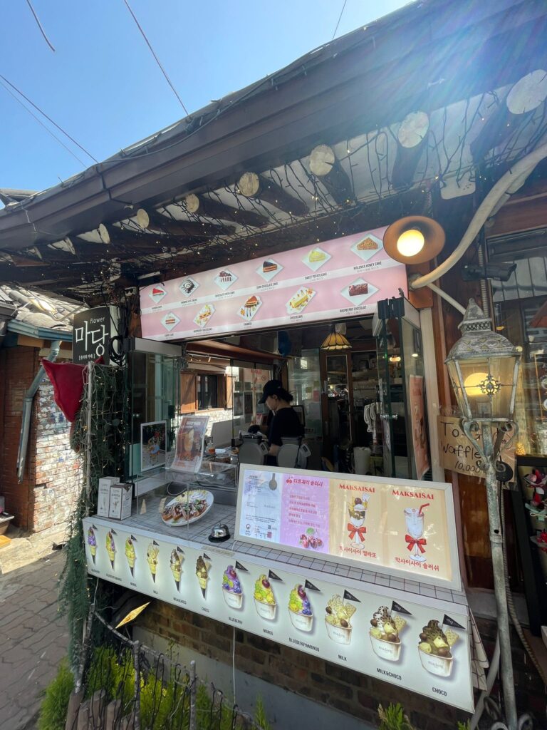 Madang Flower Cafe in Ikseon-dong Hanok Village, Seoul.

The cafe is inside a traditional Korean building (hanok) with a series of cakes listed above the counter and ice creams and fruit deserts advertised below.

The cafe is given character by fairy lights hanging from the roof and a dim lantern on the right