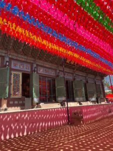 Jogyosa Temple in Seoul, South Korea. In this picture you can see the temples covered by the shadows of several red, yellow, blue, pink and green lanterns hanging above