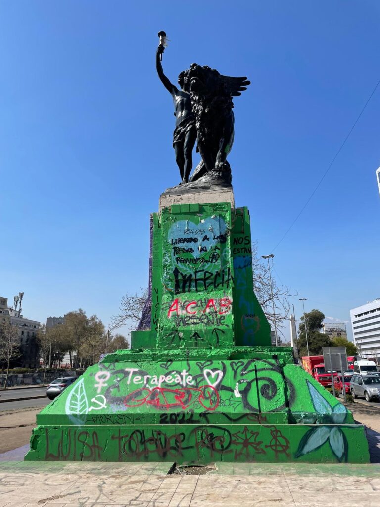 A statue in Santiago, Chile the day after violent riots. The statue stands on top of a plinth which is covered in green paint and graffiti