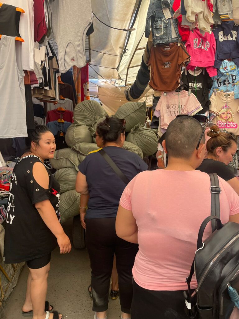 Locals shopping at Ulaanbaatar's Narantuul Market with several clothes hanging above them