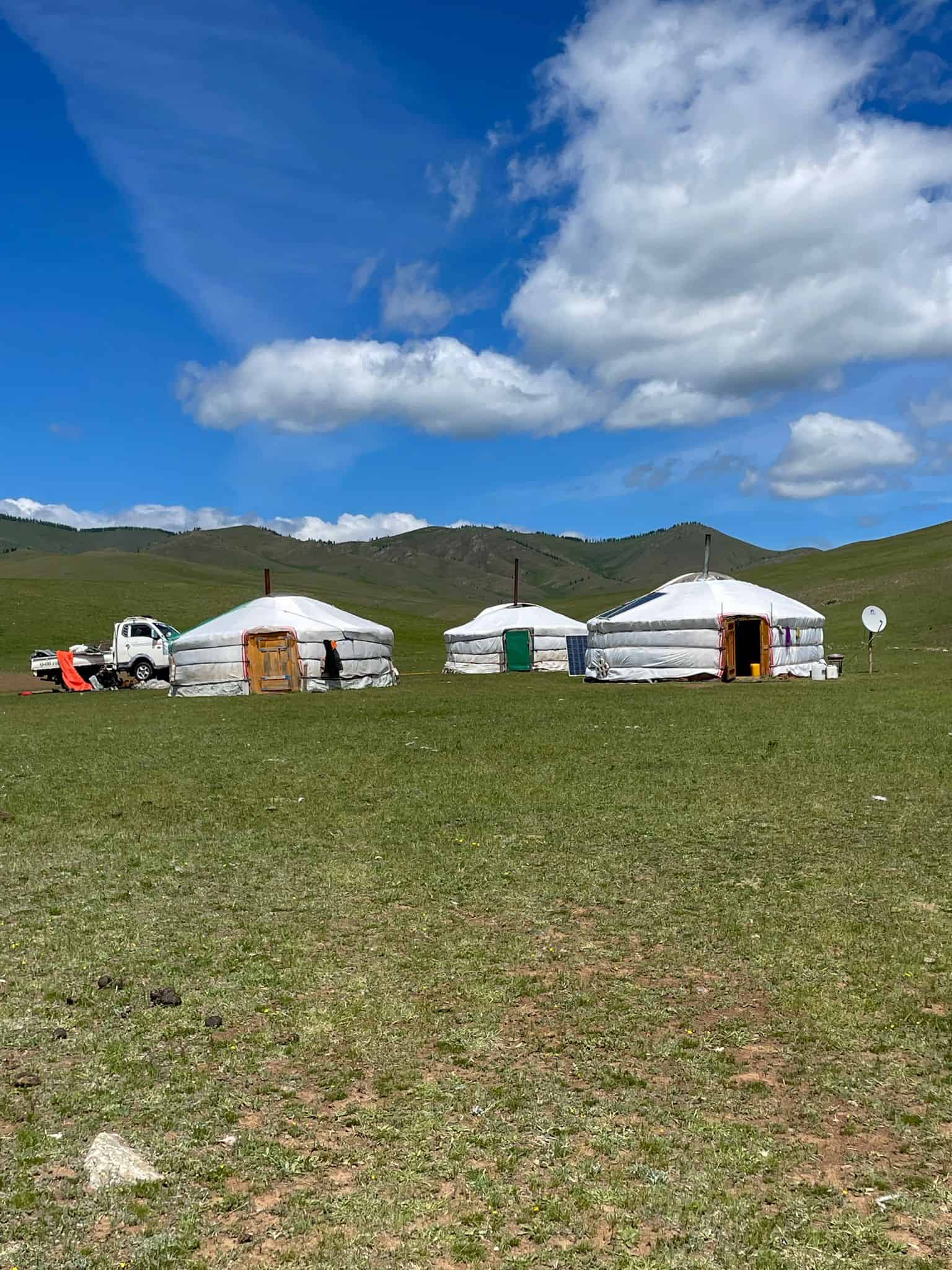 Three Mongolian gers in the countryside with the green hills of Mongolia behind them.
