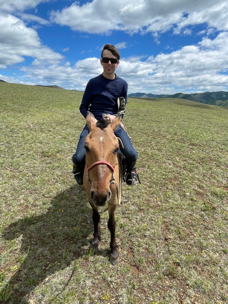 An image of me sat on horseback whilst riding through the green hills of Mongolia