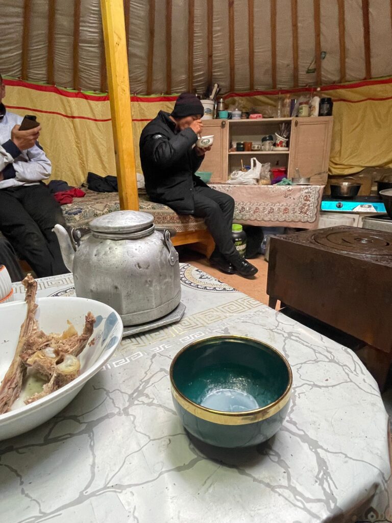 Dinner in a Mongolian ger. Lamb on the left with suutei tsai (milk tea) on the right. Our host Khatan is sat on the left (partially cut out the image) with his cousin in the centre

In the background you can see a basic kitchen space full of pots and jars