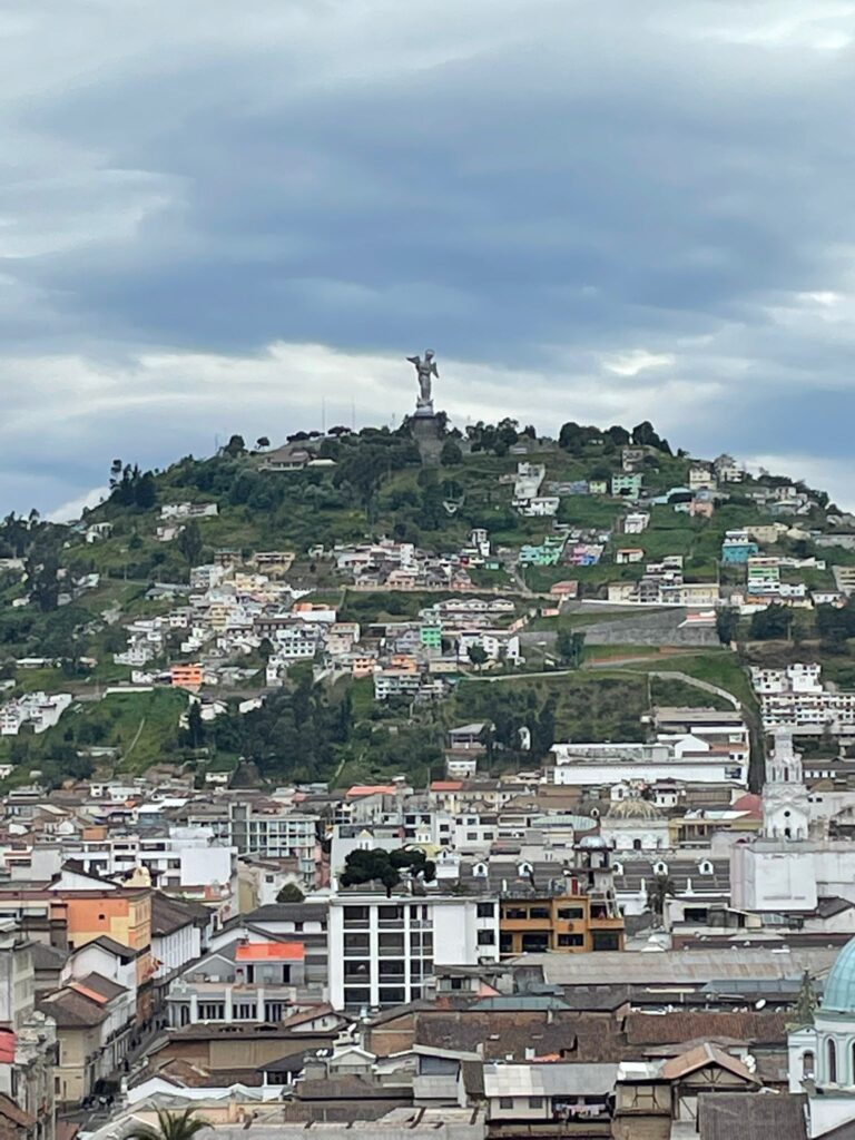 The Virgin of el Panecillo standing atop a green hill covered in small slum houses