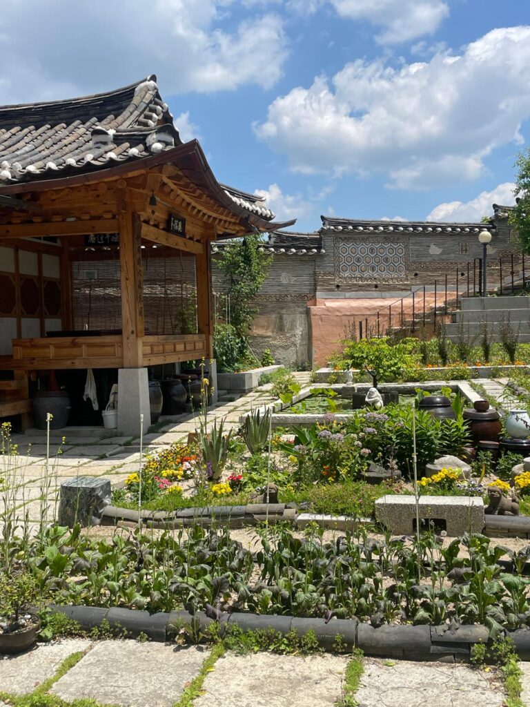 A traditional Korean hanok in Bukchon hanok village, Seoul. It is to the left of a green garden space, with a wall in the background which is also built in the traditional Korean manner