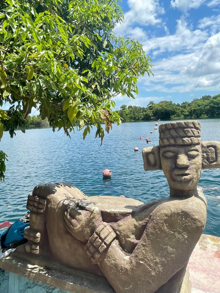 A statue beside the blue lake at Cenote Azul in Bacalar, Mexico