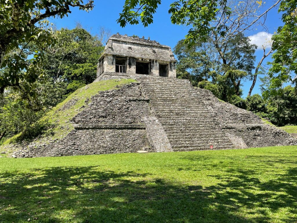 A pyramid-shaped stone temple at Palenque in Mexico. It's surrounded by green trees