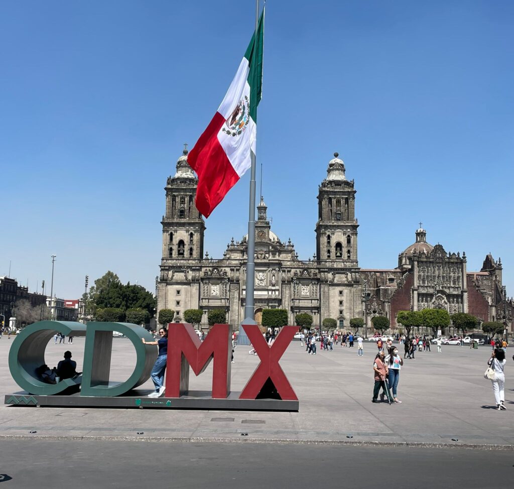 A CDMX sign in Mexico City with a Mexican flag behind it